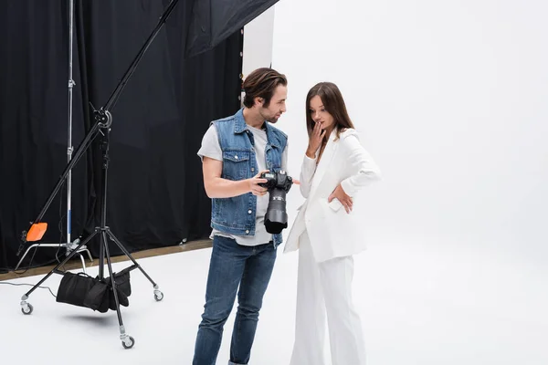 Photographer showing digital camera to surprised model covering mouth with hand in photo studio — Stock Photo