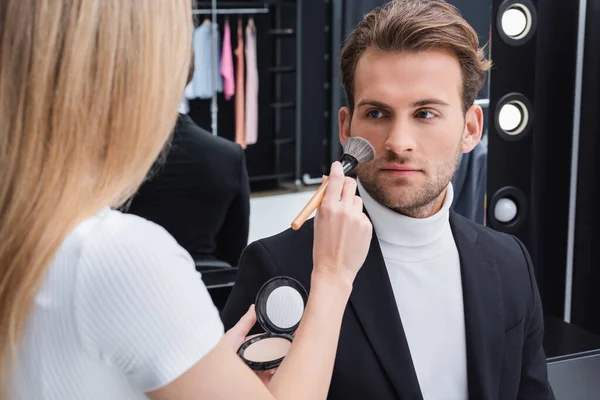 Artista visagem borrada aplicando pó rosto com escova cosmética no homem no estúdio de fotografia — Fotografia de Stock