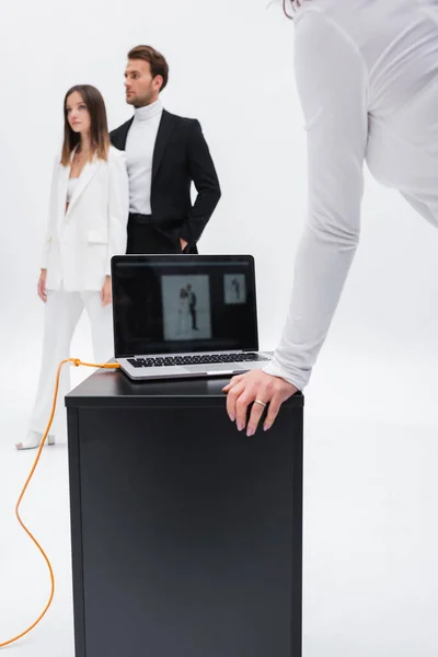 Verschwommene Models in Anzügen posieren in der Nähe von Art Director und Laptop isoliert auf weiß — Stockfoto