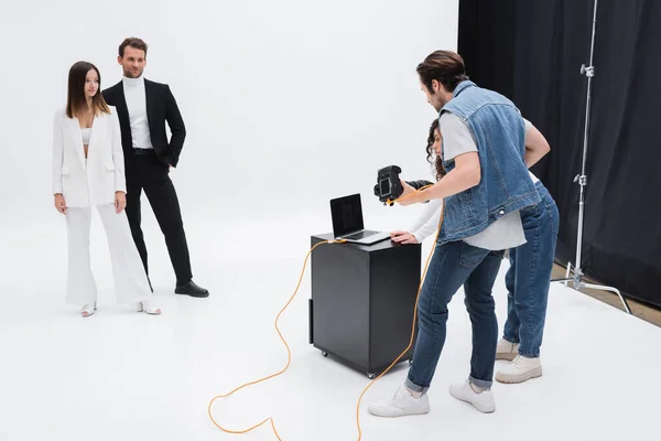 Art director with photographer looking at laptop with blank screen near models in photo studio on white — Stock Photo