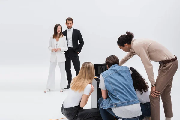 Modelos em roupas elegantes de pé perto da equipe olhando para laptop no estúdio de fotos em branco — Fotografia de Stock