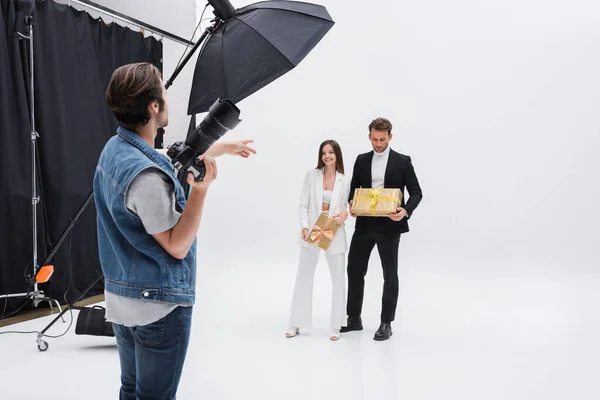 Photographe pointant vers les modèles tenant des boîtes-cadeaux sur blanc — Photo de stock