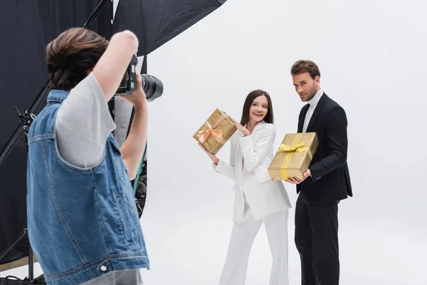 Modelos alegres posando con cajas de regalo cerca de fotógrafo trabajando en estudio de fotos - foto de stock