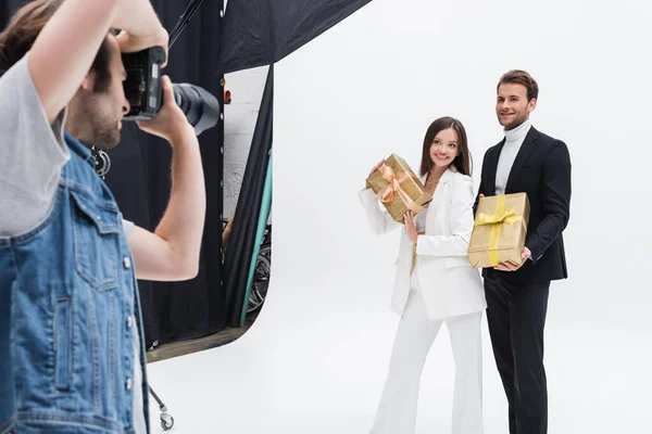 Blurred photographer taking picture of smiling models with gift boxes on white — Foto stock