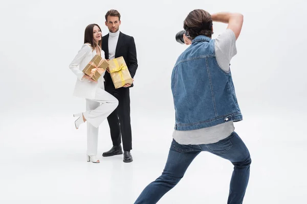 Vista posteriore di fotografo professionista scattare foto di modelli alla moda con scatole regalo su bianco — Foto stock