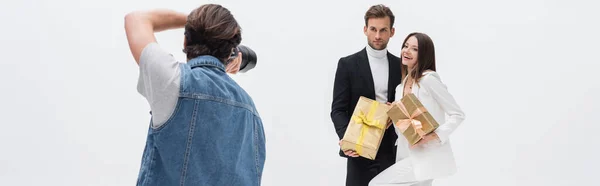 Back view of photographer taking photo of stylish models with gift boxes isolated on white, banner — Foto stock