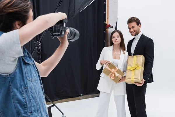Modelos elegantes que sostienen cajas de regalo mientras posan en el fotógrafo en el estudio de fotos - foto de stock
