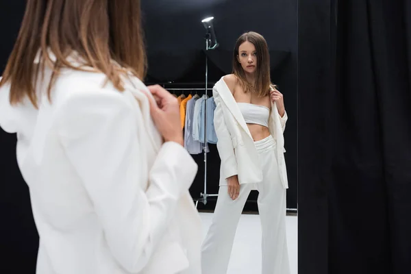 Брюнетка модель в білому костюмі позує біля дзеркала в фотостудії — стокове фото