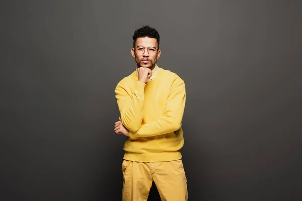 Serious african american man in yellow outfit and glasses looking at camera on dark grey — Stock Photo