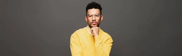 Hombre afroamericano serio en traje amarillo y gafas mirando a la cámara aislada en gris, pancarta - foto de stock