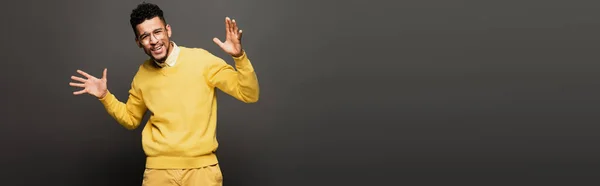 Hombre afroamericano feliz en traje amarillo y gafas gestos en gris oscuro, bandera - foto de stock