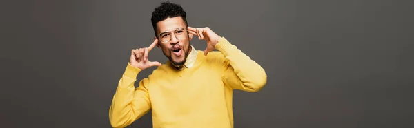 Sorprendido hombre afroamericano en traje amarillo y gafas aisladas en gris, pancarta - foto de stock