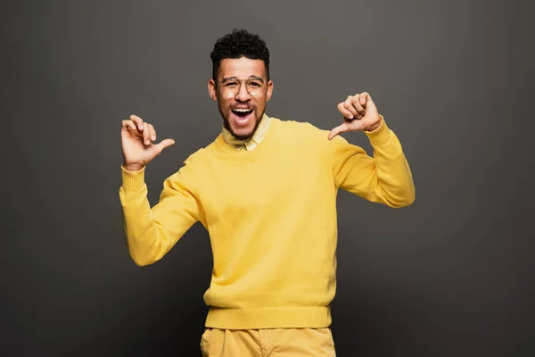 Positivo afro americano uomo in occhiali puntando con i pollici a se stesso su grigio scuro — Foto stock