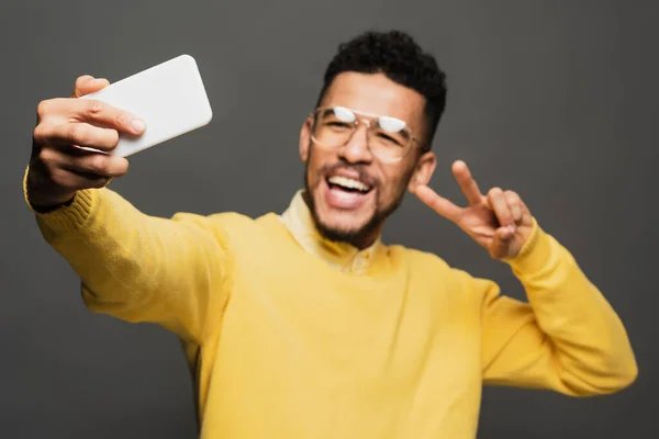 Blurred excited african american man in glasses taking selfie isolated on grey — Stock Photo