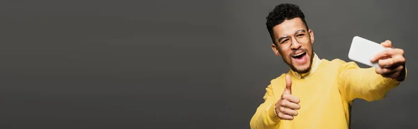 Young excited african american man in glasses taking selfie isolated on grey, banner — Stock Photo