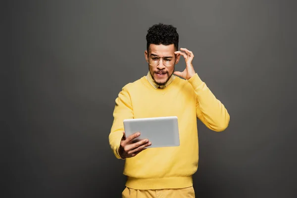 Thoughtful african american man in glasses using digital tablet on dark grey — Stock Photo