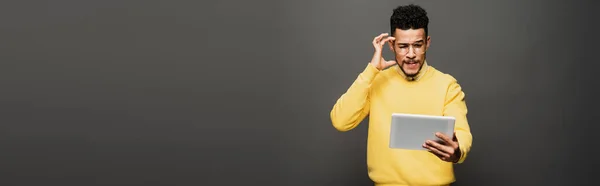 Thoughtful african american man in glasses using digital tablet on dark grey, banner — Stock Photo