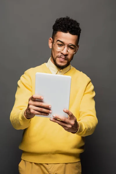 Displeased african american man in glasses using digital tablet isolated on grey — Stock Photo