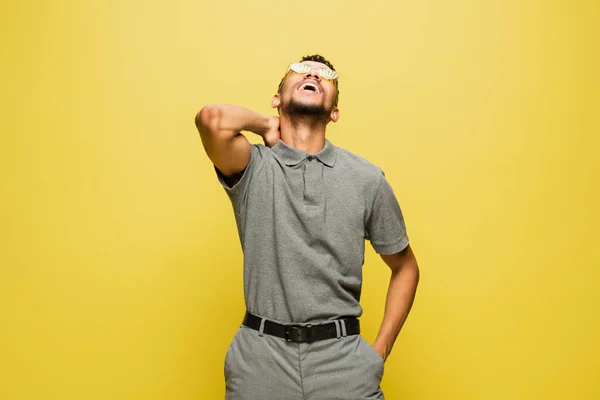 Joyeux homme afro-américain en lunettes de soleil et chemise de tennis grise riant isolé sur jaune — Photo de stock