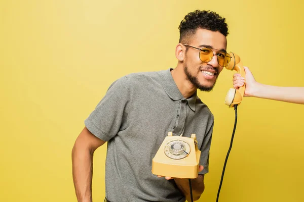 Femme tenant combiné près de joyeux homme afro-américain en lunettes de soleil et chemise de tennis grise sur jaune — Photo de stock