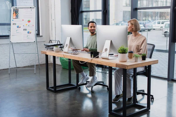 Задоволені міжрасові колеги дивляться один на одного під час роботи в сучасному офісі — стокове фото