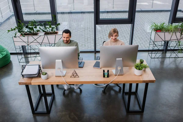 Vista de ángulo alto de colegas interracial que trabajan en la oficina moderna - foto de stock