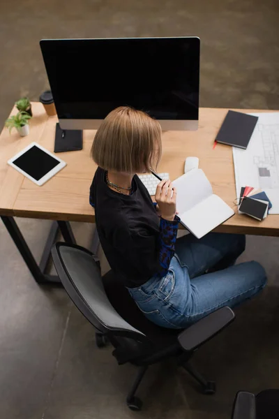 Visão de alto ângulo de designer de interiores loira segurando notebook perto de dispositivos na mesa — Fotografia de Stock