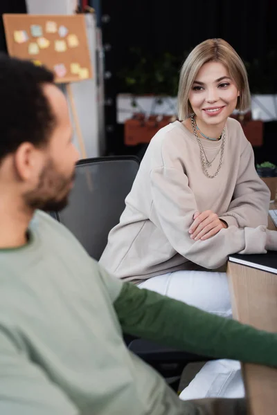 Cheerful woman looking at blurred african american colleague — Stock Photo