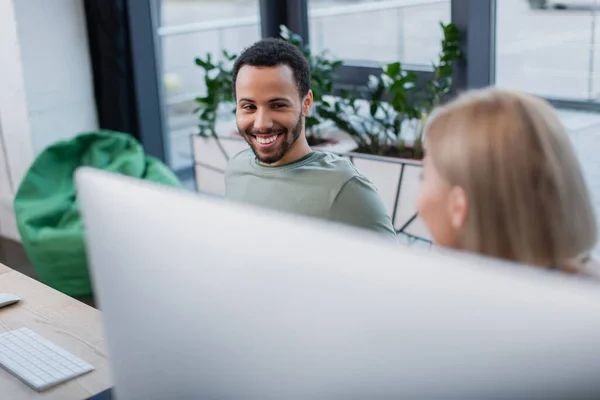 Happy african american man looking at blonde colleague in office — Stock Photo