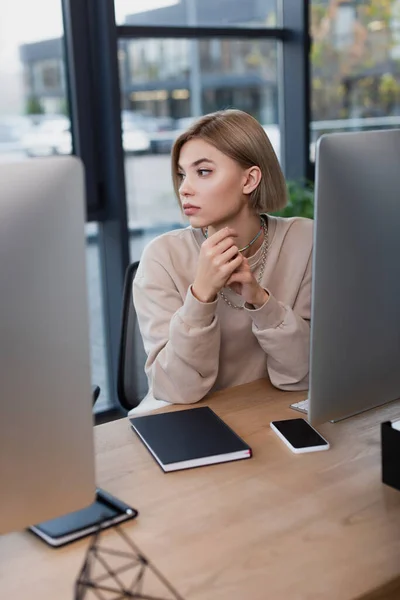 Joven gerente rubia trabajando cerca de monitores de ordenador en la oficina moderna — Stock Photo