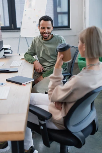 Alegre africano americano manager mirando rubia colega con papel taza - foto de stock