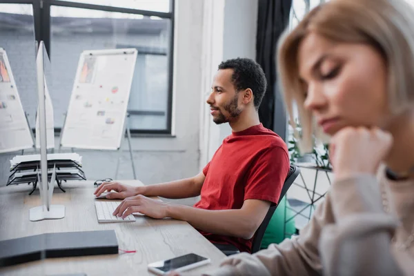 Africano americano manager escribiendo en teclado cerca borrosa colega - foto de stock