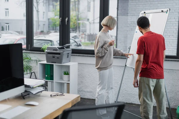 Collègues interracial à la recherche de tableau à feuilles mobiles dans le bureau moderne — Photo de stock