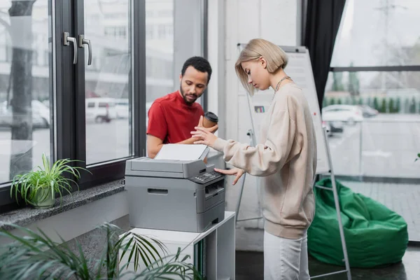 Blondine kopiert Dokument bei afrikanisch-amerikanischem Manager mit Pappbecher — Stockfoto