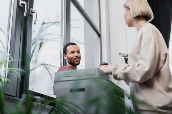 Blonde woman looking at african american manager near printer — Stock Photo