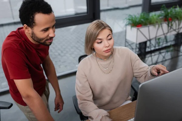 High angle view of blonde manager pointing at computer monitor near african american colleague — Stock Photo