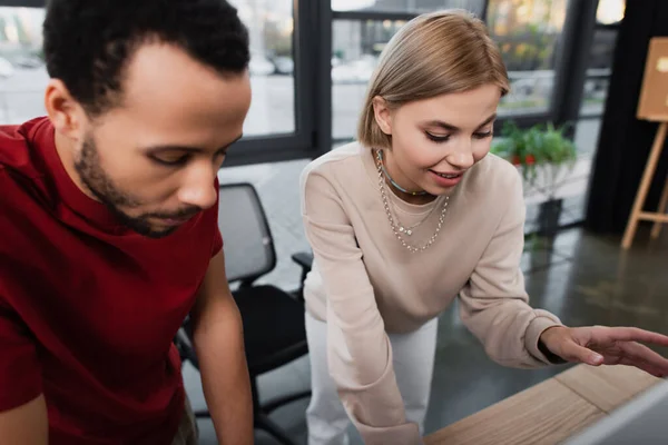 Mujer de negocios rubia sonriendo y haciendo gestos cerca de un colega afroamericano - foto de stock