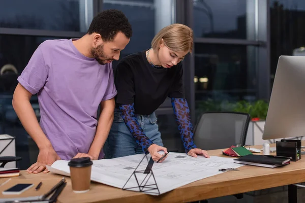 Young multiethnic colleagues looking at blueprint on desk — Stock Photo