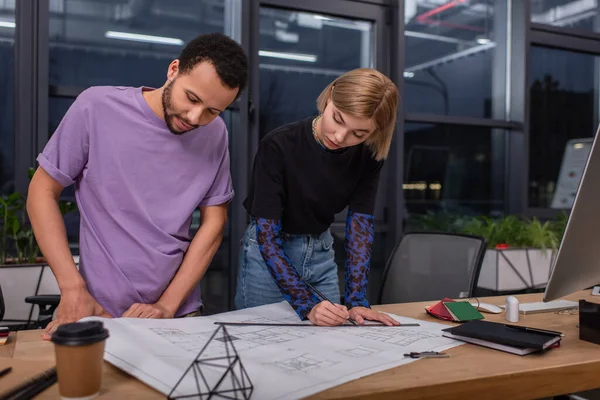 Jóvenes diseñadores de interiores multiétnicos mirando el plano en el escritorio - foto de stock