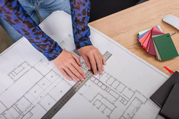 Top view of interior designer holding ruler while working with blueprint near colorful samples — Stock Photo