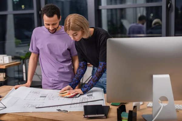 Interracial interior designers looking at colorful samples near blueprint — Stock Photo