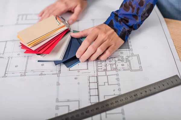 Cropped view of interior designer holding colorful samples near blueprint — Stock Photo