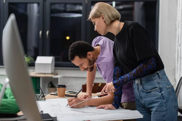 Young multiethnic interior designers working with blueprint in office — Stock Photo