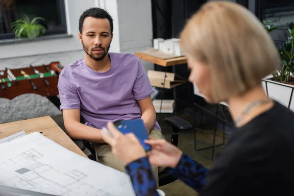 Africano americano interior designer guardando offuscata bionda collega con campione — Foto stock