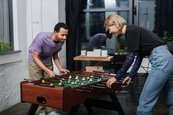 Africano americano manager jugando fútbol de mesa con feliz rubia colega - foto de stock