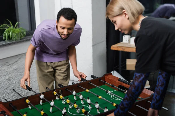 African american manager playing table football with blurred blonde colleague — Stock Photo