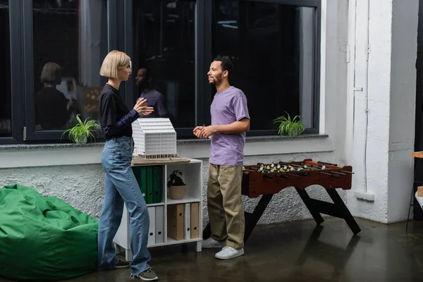 Full length of interracial colleagues talking near table football in office — Stock Photo