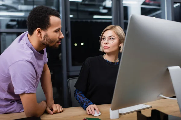 Blonde Managerin in Brille mit Computer in der Nähe eines amerikanischen Kollegen — Stockfoto