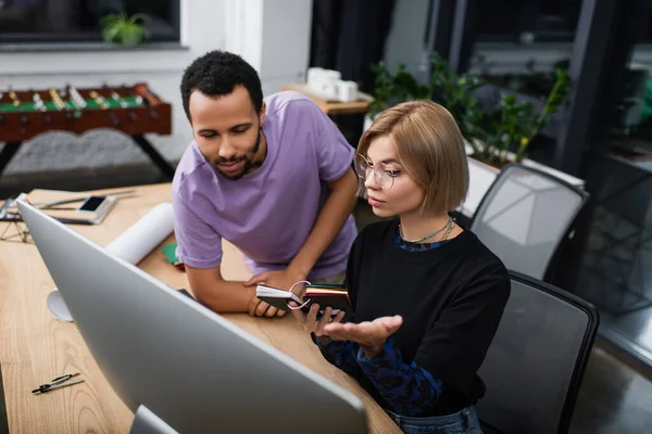 Blonde interior designer in glasses holding colorful samples near african american colleague — Stock Photo