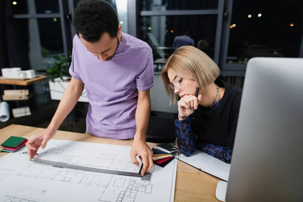 African american interior designer using ruler near blueprint and blonde colleague in glasses — Stock Photo